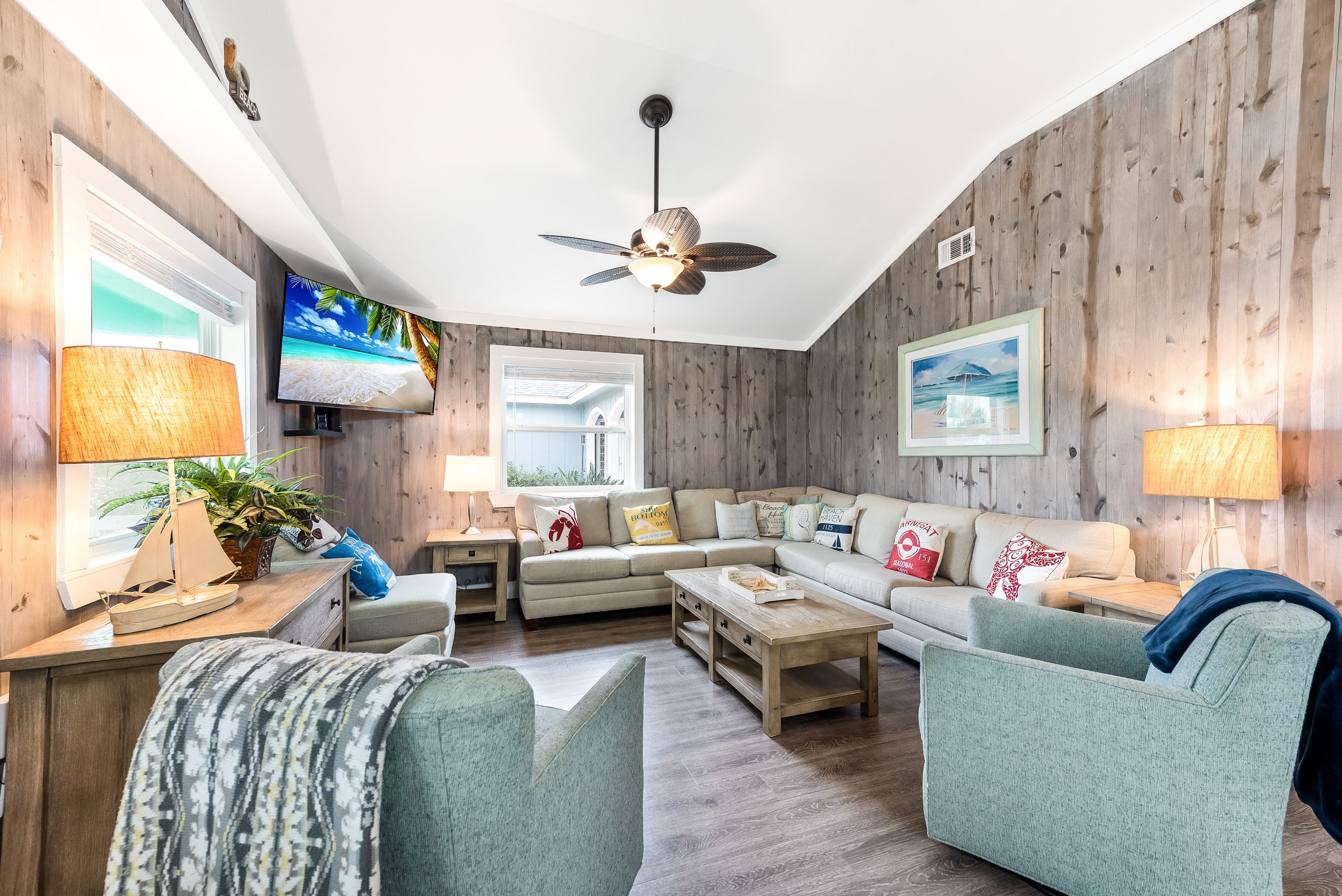 A cozy living room with a sectional sofa, a coffee table, and a ceiling fan.