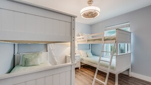 A room with bunk beds, a ladder, a nightstand, and a window with blinds. - Diving Dolphin by Silver Sands Vacation Rentals (Port Aransas)