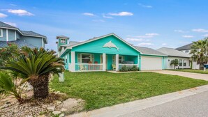A turquoise house with a white porch and a garage. - Diving Dolphin by Silver Sands Vacation Rentals (Port Aransas)