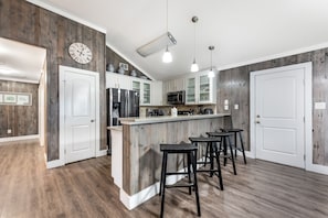 Cozinha moderna com paredes de madeira, armários brancos, uma ilha central com banquetas e um relógio na parede.