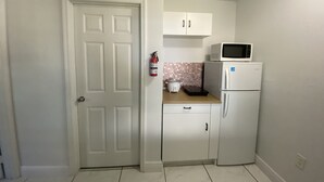Una cucina compatta con mobili bianchi, un forno a microonde, un frigorifero e un piccolo piano di lavoro con una slow cooker.
