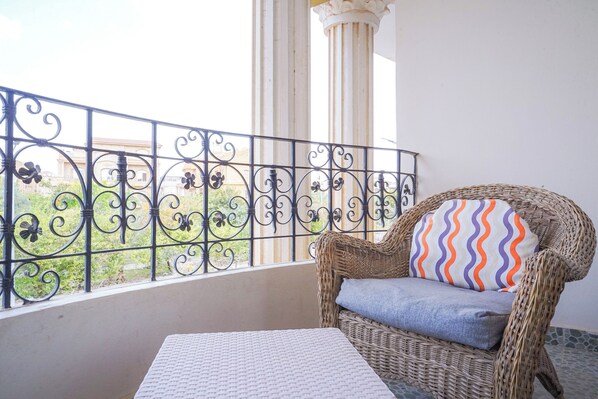 Un balcon avec un fauteuil en osier, un coussin à motifs et une table.