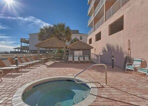 A rooftop pool area with lounge chairs, a hot tub, and a covered seating area.
