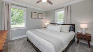 A bedroom with a large bed, two bedside tables, a ceiling fan, and two windows with curtains.