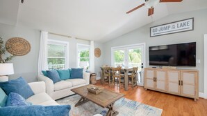 A living room with a sofa, coffee table, TV, wooden cabinet, dining table, chairs, and a ceiling fan.