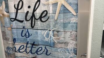 A bathroom with a shower curtain featuring a beach theme, including text and sea creature illustrations.
