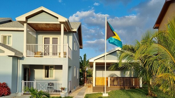 A two-story building with a balcony, a flag, and tropical plants.