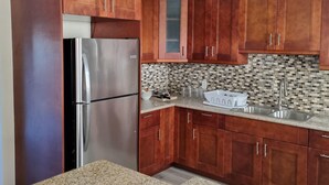 A kitchen with wooden cabinets, a stainless steel refrigerator, a tiled backsplash, and a granite countertop.