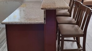 A kitchen with a granite countertop, wooden chairs, and a built-in wooden cabinet above the counter.