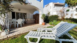 A patio with white lounge chairs, a table, and a sofa under a white building with an archway. - São Rafael Beach House (Albufeira)
