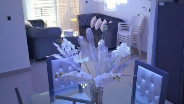 Un comedor con una mesa de vidrio, sillas blancas y un florero con flores blancas.