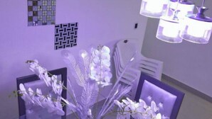 Un comedor con una mesa de vidrio rodeada de sillas, un jarrón con flores blancas y decoraciones de pared estampadas.