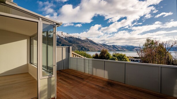 A balcony with a wooden floor and a glass door, overlooking a lake and mountains.