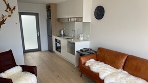 A modern living room with a brown leather sofa and a white furry throw. A kitchen with white cabinets and stainless steel appliances is visible in the background.