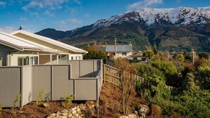 A modern house with a large balcony, surrounded by a stone wall and a view of snow-capped mountains.