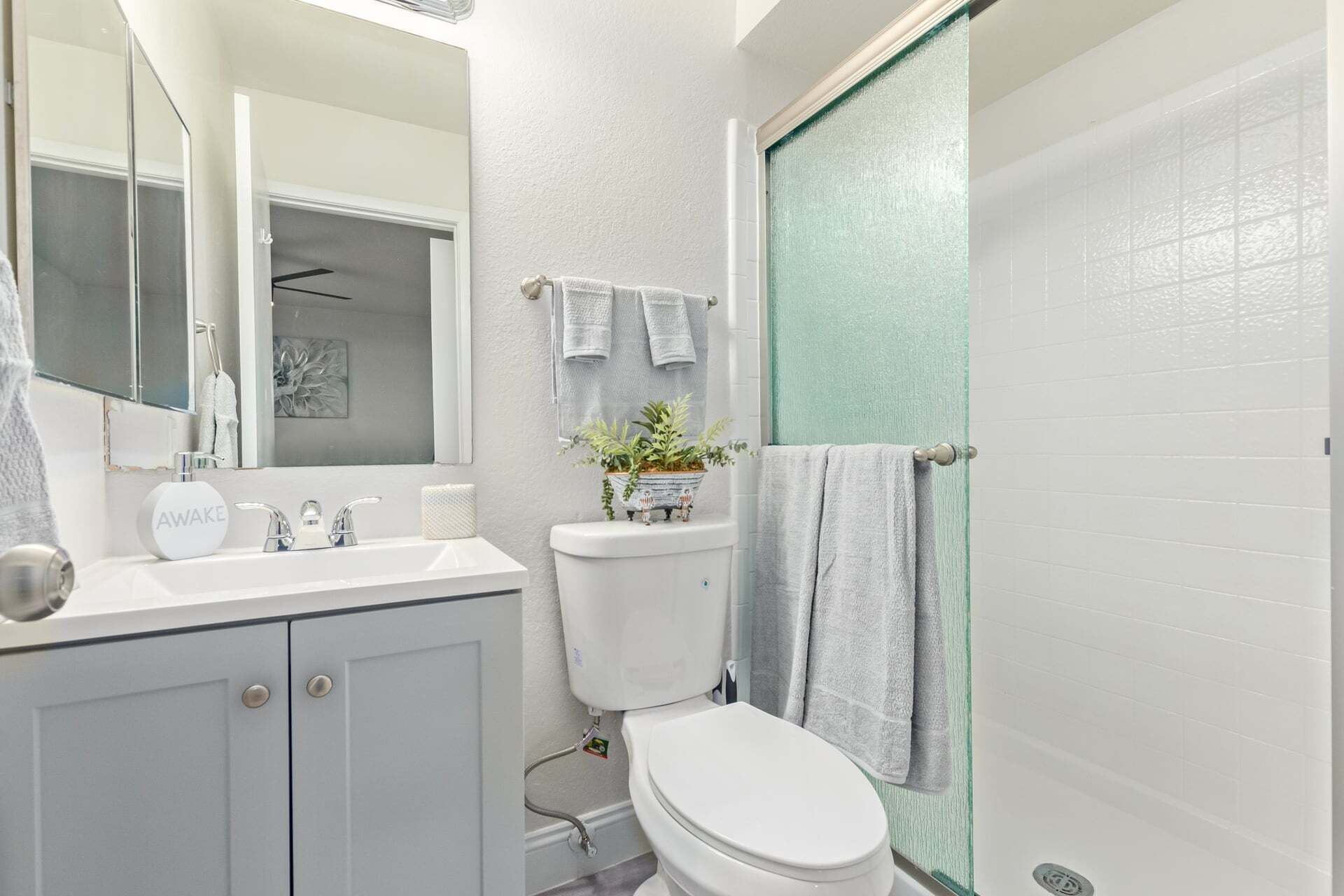 A bathroom with a toilet, sink, mirror, and shower.