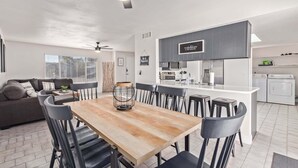 A modern kitchen with dark cabinets, a central island, and a dining area with a wooden table and black chairs.