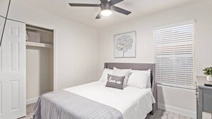 A bedroom with a bed, a ceiling fan, a window with blinds, and a door.