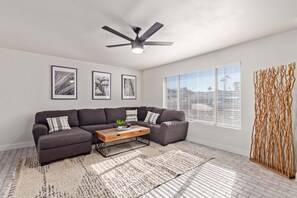 A living room with a sectional sofa, a coffee table, a ceiling fan, and a large window with blinds. - Stunning Hunter Single Family Home in the Heart of Mesa (Mesa)