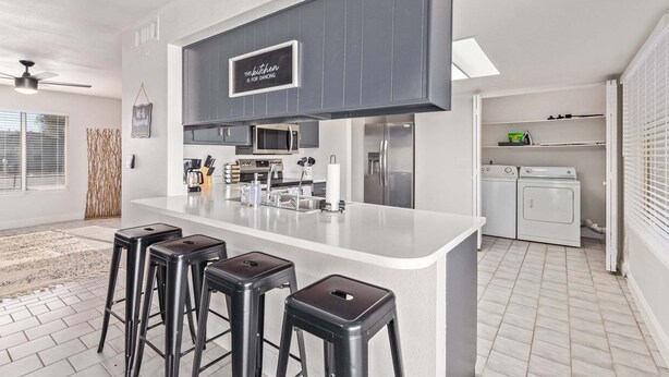 A modern kitchen with a central island, bar stools, a microwave, a refrigerator, and a washing machine.