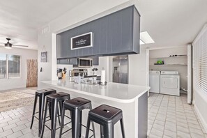 A modern kitchen with a central island, bar stools, a microwave, a refrigerator, and a washing machine. - Stunning Hunter Single Family Home in the Heart of Mesa (Mesa)