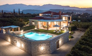 Una casa moderna de dos pisos con piscina, mobiliario exterior y vistas a montañas.