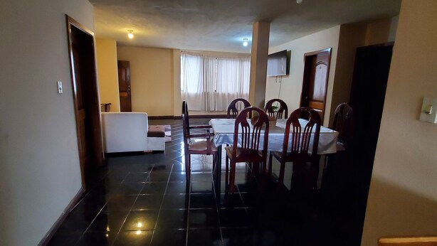 A dining area with a table and chairs, a sofa, and a TV mounted on the wall. - Apartamento 3 habitaciones y parqueo (Cuenca)
