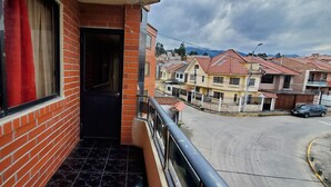 A balcony with a view of a residential street, a black door, and a red curtain. - Apartamento 3 habitaciones y parqueo (Cuenca)