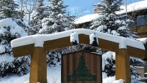 Un arco de madera con un letrero que dice "Redpine Clubhouse" rodeado de árboles cubiertos de nieve y un edificio al fondo.