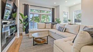 A modern living room with a sectional sofa, a coffee table, and a flat-screen TV mounted on the wall.