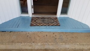 Een blauwe veranda met een welkomstmat en een betonnen trap naar een deur.