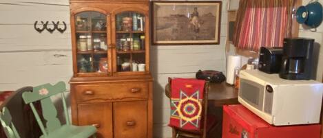 A compact kitchen with a wooden cabinet, a red refrigerator, a microwave, a chair, and a patterned rug.