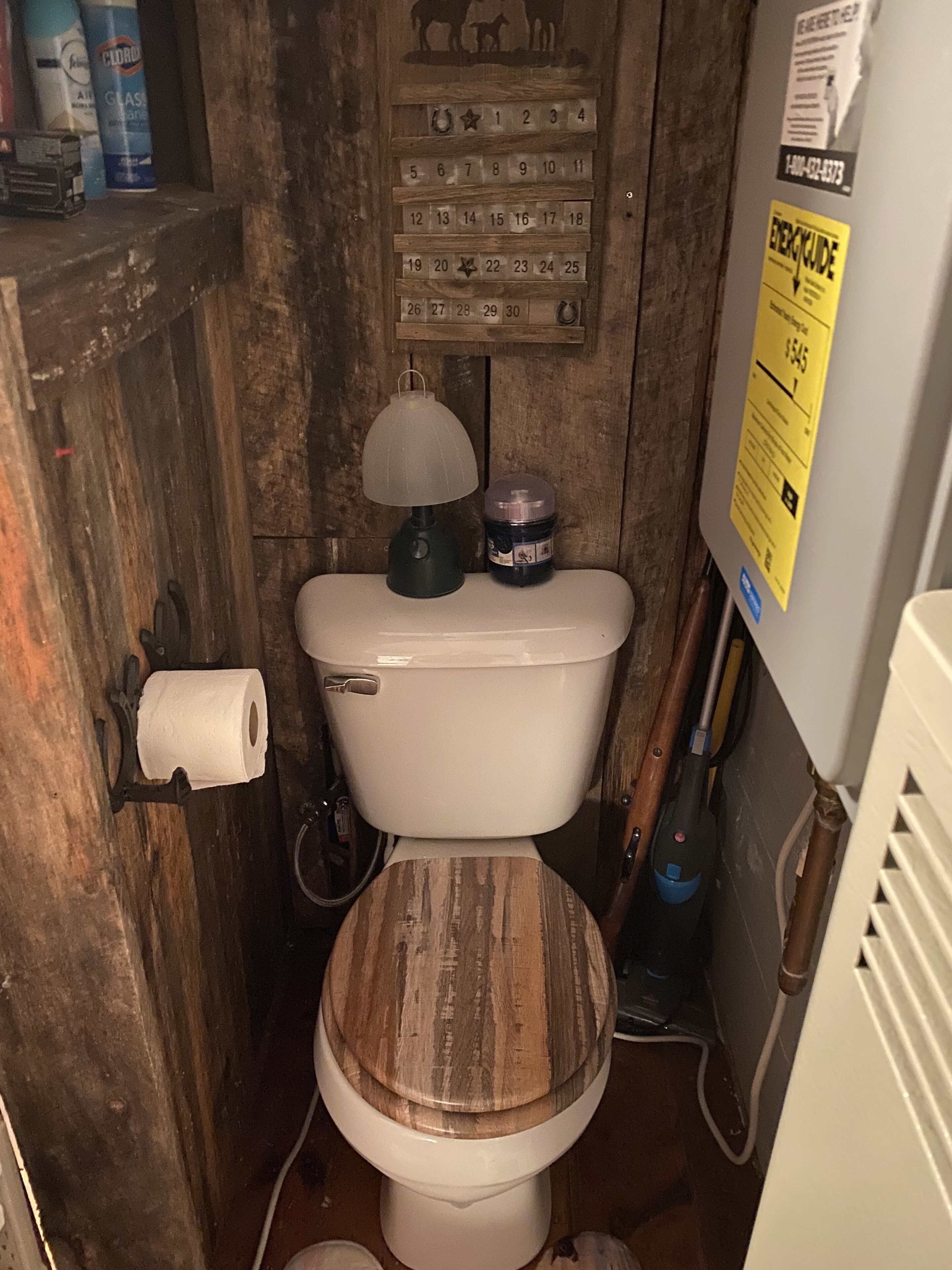 Un baño rústico con un asiento de inodoro de madera, un calendario y un dispensador de papel higiénico.