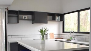 A modern kitchen with a large island, black cabinetry, and a window providing natural light. - Blue Window (Veintisiete de Abril)