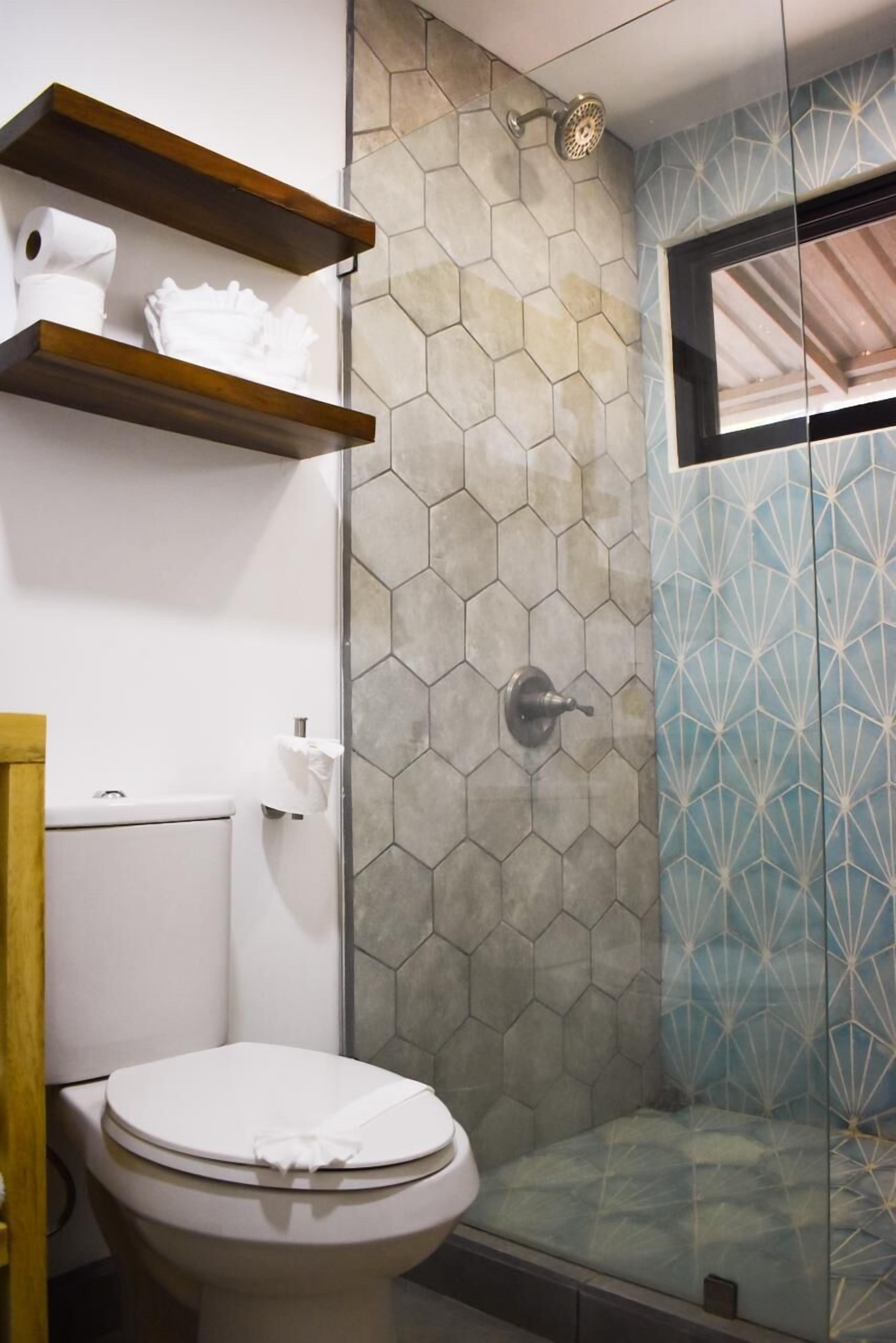 A bathroom with a toilet, a shower with a glass door, and wooden shelves above the toilet.