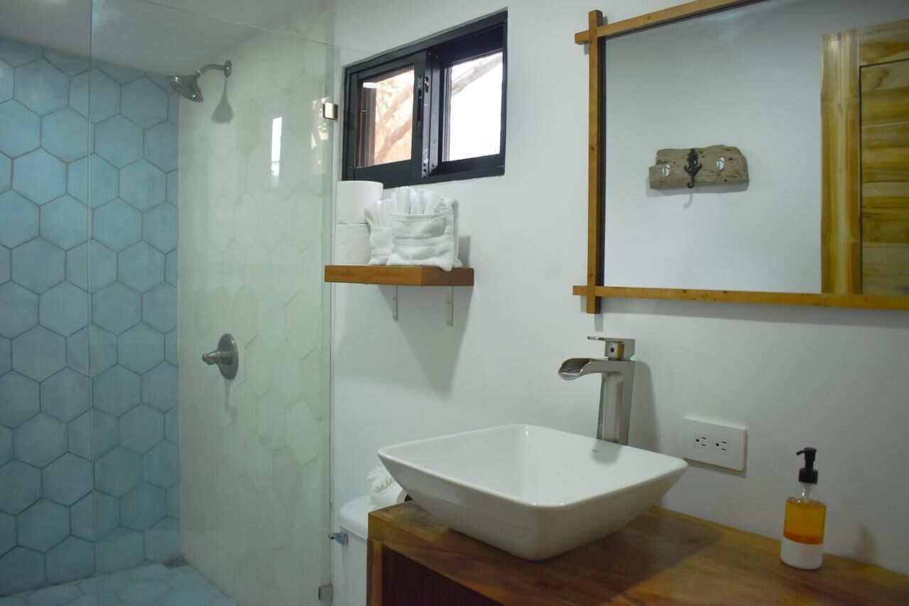 A bathroom with a white sink, a wooden shelf with towels, a window, and a mirror.