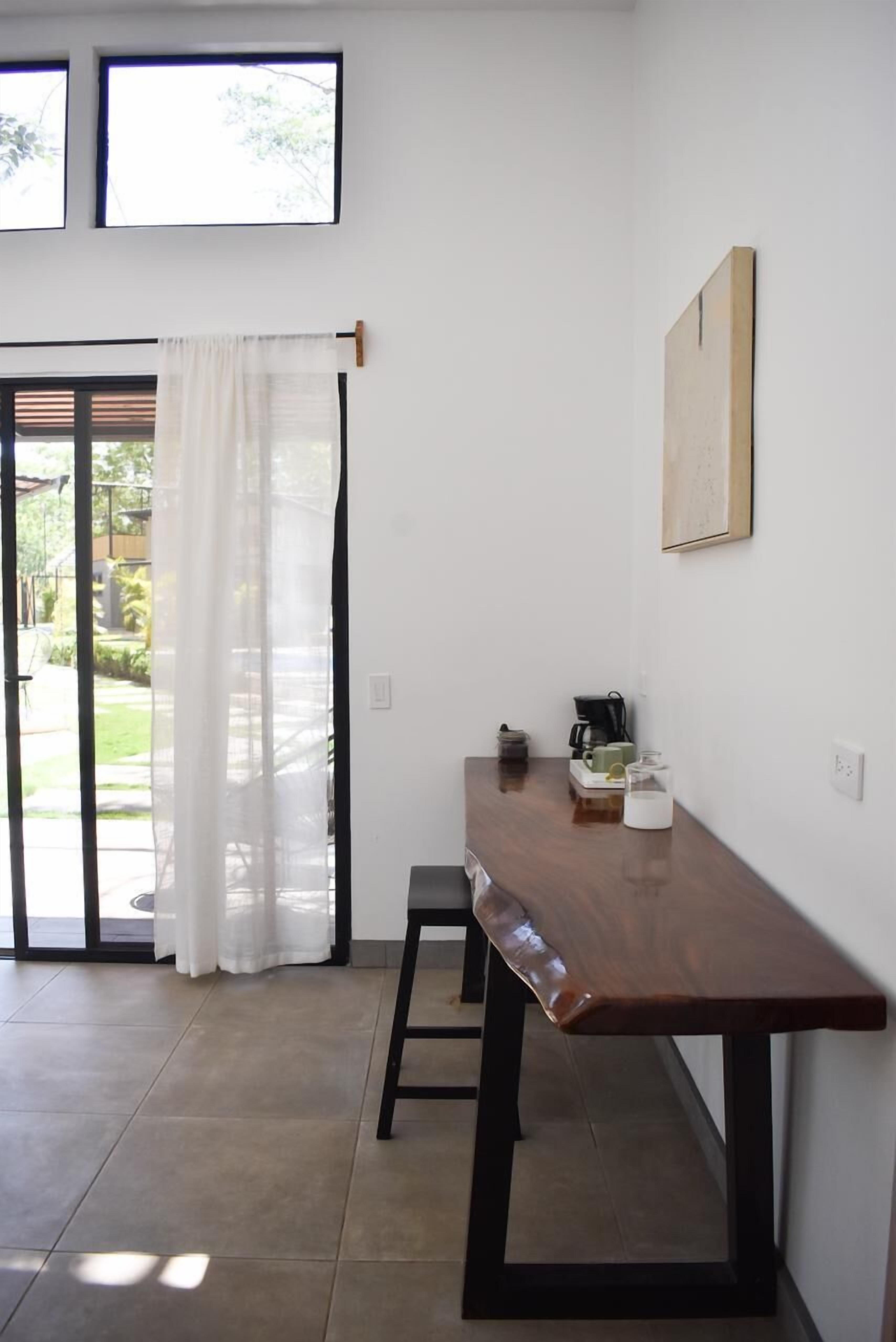 A small, modern kitchen with a wooden table, a coffee maker, and a view through a glass door to an outdoor area.
