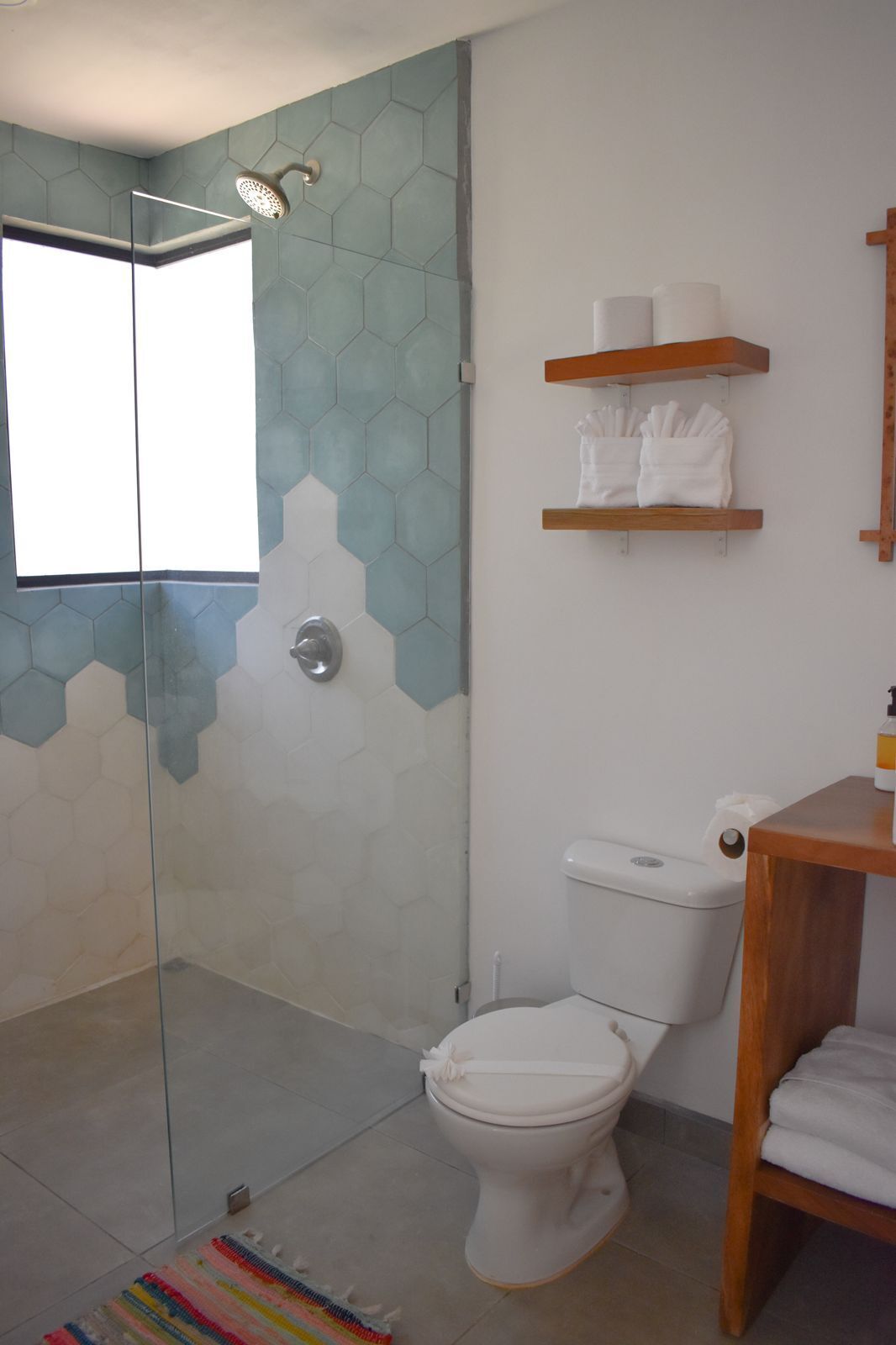 A bathroom with a glass-enclosed shower, a toilet, and a wooden shelf with towels.