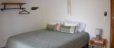 Une chambre à coucher avec un lit, une table de chevet avec une lampe, un porte-manteau et un attrape-rêves fixé au mur.