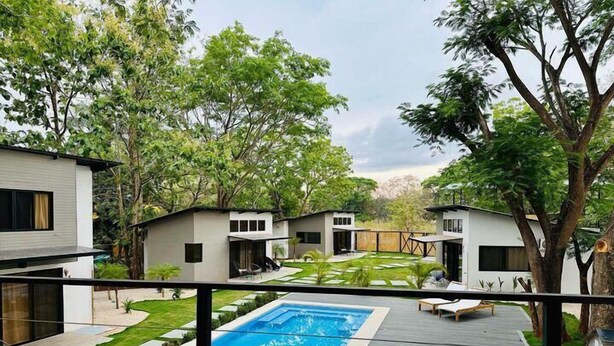 A modern outdoor pool area with a wooden deck, lounge chairs, and a view of adjacent buildings. - Blue Window (Veintisiete de Abril)