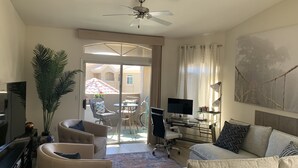 A living room with a sofa, armchairs, a TV, a desk with a computer, and a balcony with a table and chairs. - Paradise Valley area condo with heated pool and gym,  near Mayo Clinic. (Scottsdale)