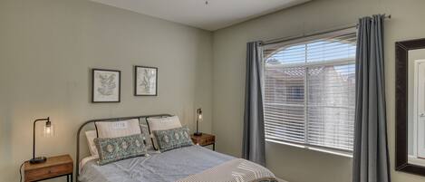 A bedroom with a bed, nightstands, a ceiling fan, a window with curtains, and framed artwork on the wall.