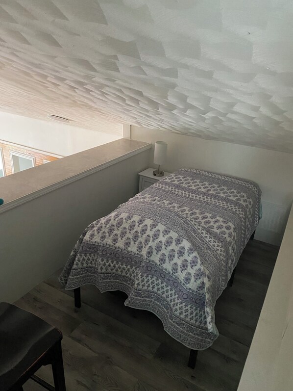 Une petite pièce agréable, avec un lit, une table de chevet, une lampe et une fenêtre.