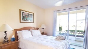 Habitación de hotel con una cama grande, dos mesitas de noche, un ventilador de techo, una ventana con vistas y un cuadro en la pared.