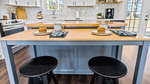 A modern kitchen with a central island, two black stools, and a coffee maker. - Quiet and Cozy with Outdoor Space (Duncan)
