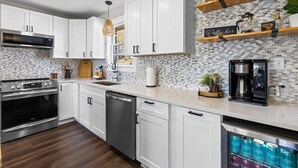 A modern kitchen with white cabinets, a stainless steel oven, a dishwasher, and a coffee machine. - Quiet and Cozy with Outdoor Space (Duncan)