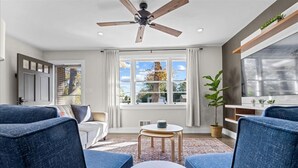 A modern living room with a ceiling fan, large windows, a sofa, a coffee table, and a potted plant. - Quiet and Cozy with Outdoor Space (Duncan)