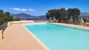 A rectangular swimming pool with a clear blue water surface, surrounded by a beige deck. In the background, there are trees and a mountainous landscape under a clear blue sky. - 2 bedroom lovely home in Grosseto-Pugna (Grosseto-Pugna)