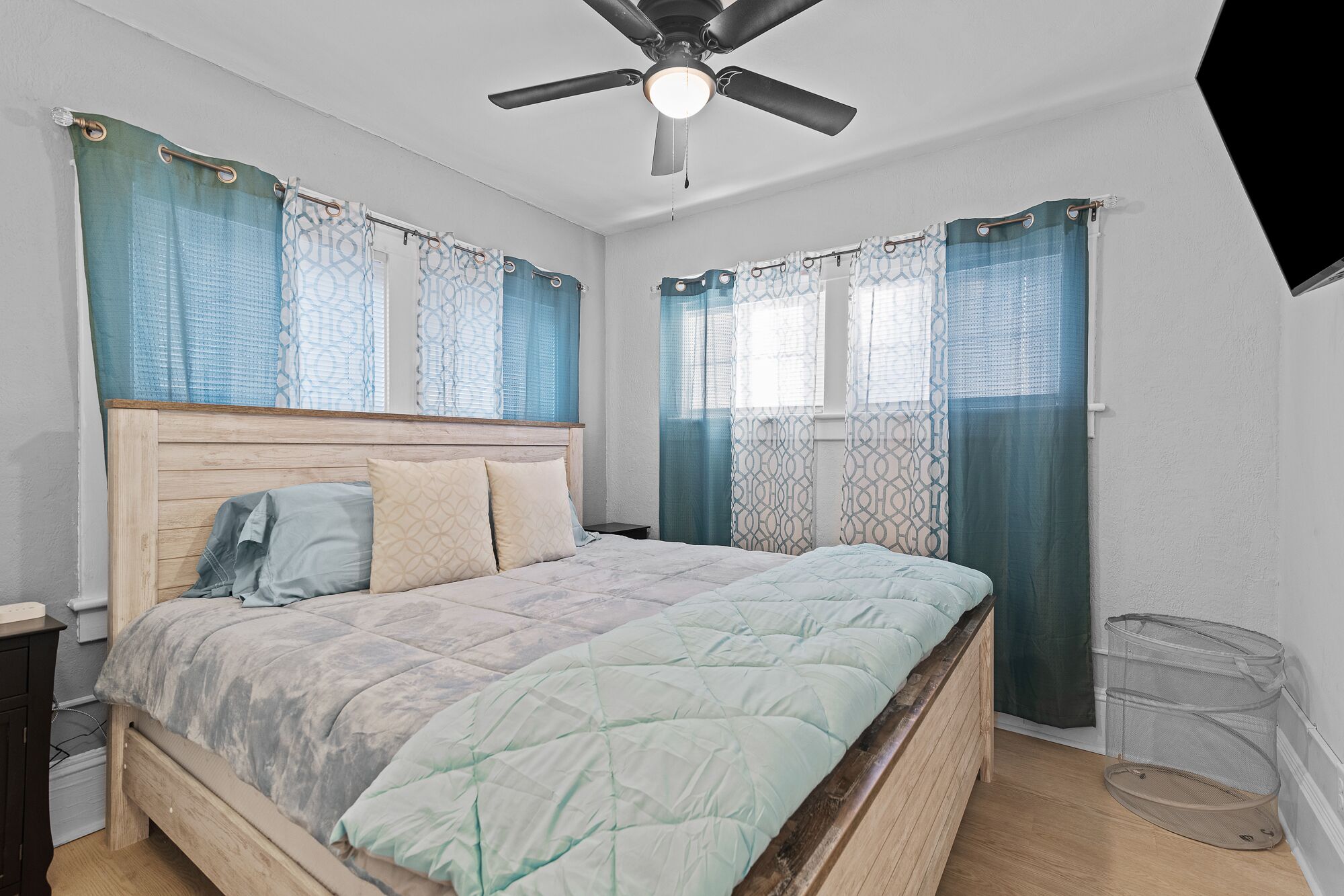 A bedroom with a wooden bed, a ceiling fan, and a window with curtains.