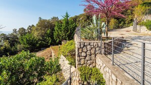 A stone retaining wall with metal railings, surrounded by lush greenery and a pink flowering tree. - Beautiful apartment in Moscenicka Draga (Moscenicka Draga)